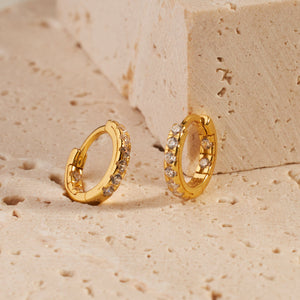 The crystal accents on the inner and outer curves of a pair of Santorini Huggie earrings sparkle against the shining golden hoops.