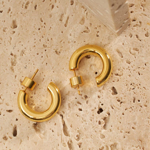 A pair of Perfect Hoop Mini earrings lay on a porous stone slab, showing off the open hoop design and cylindrical push-back closure.