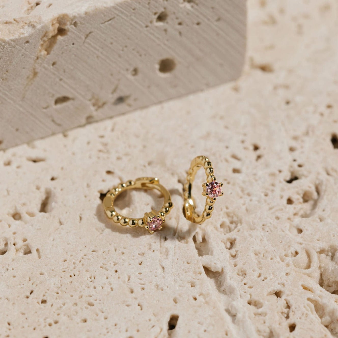 A pair of Bambina Cristallo Huggie earrings sits on display, one laying on its side while the other is propped up to show off the bubble texture and crystal accent. 