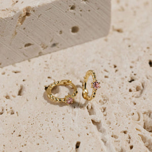 A pair of Bambina Cristallo Huggie earrings sits on display, one laying on its side while the other is propped up to show off the bubble texture and crystal accent. 