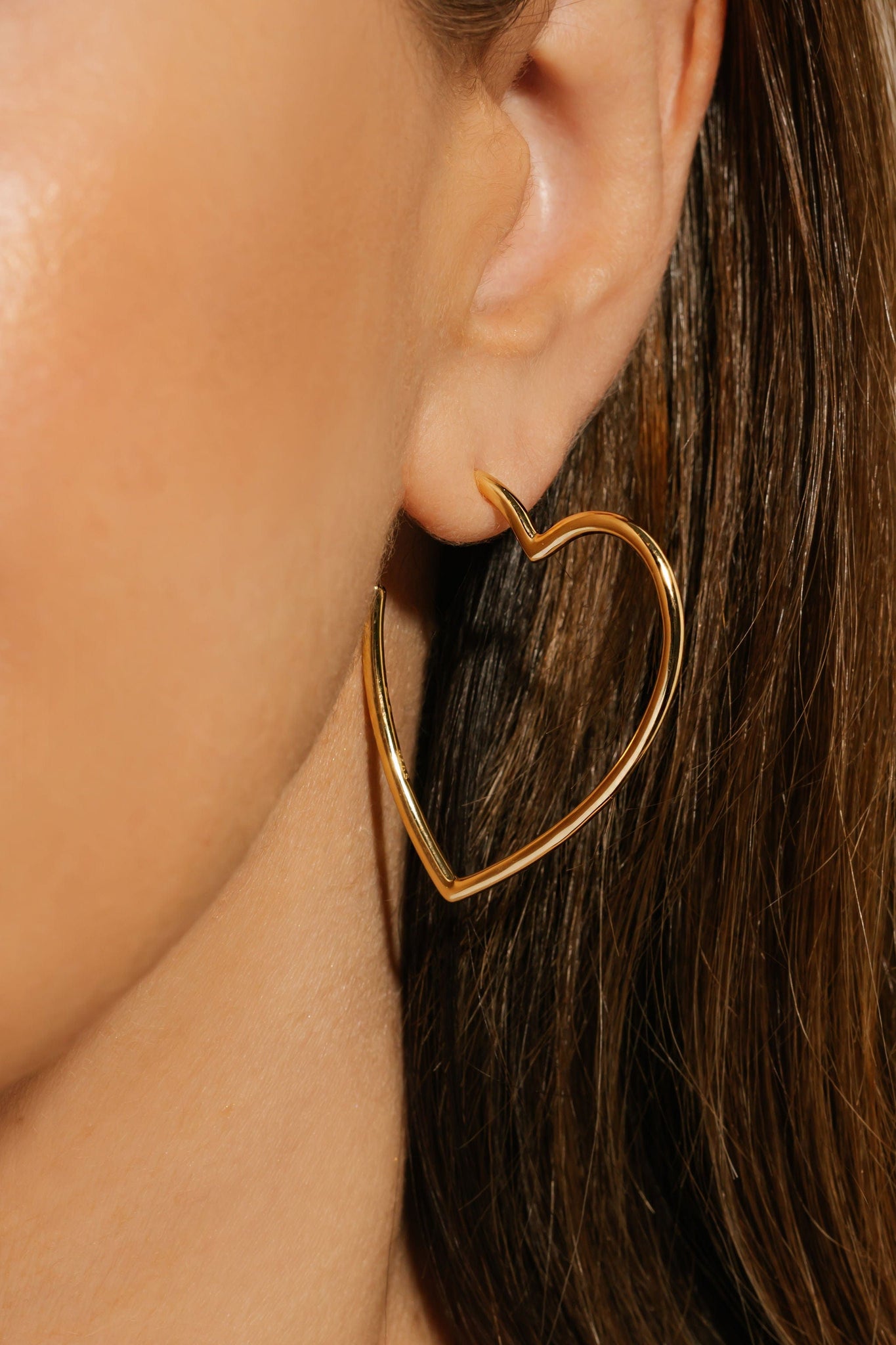 The open heart shape and golden shine of the Amore Hoop earring gracefully adorn the model's ear.