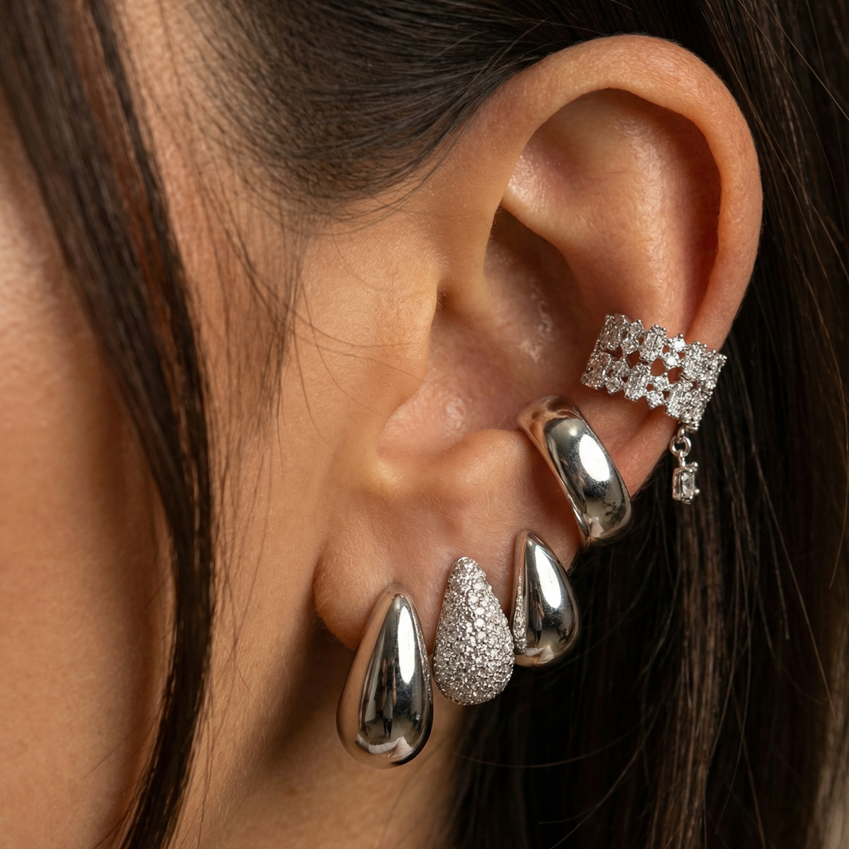 A pair of platinum open hoop earrings sits on stone slabs, one earring standing on its curve, the other sideways on a block. 
