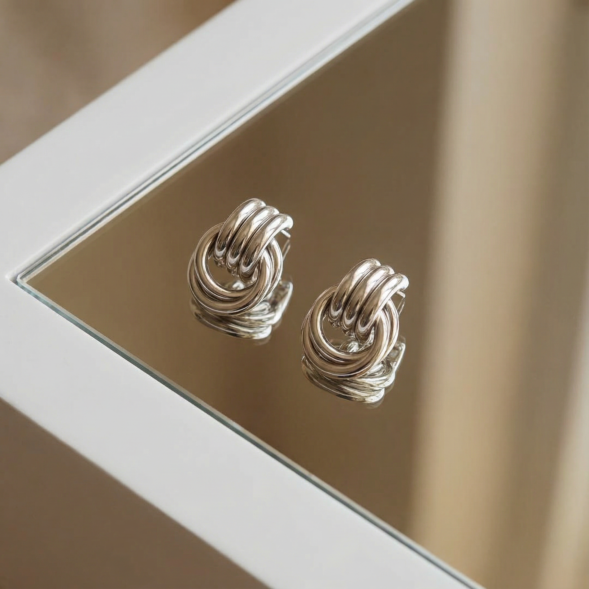A pair of platinum open hoop earrings sits on stone slabs, one earring standing on its curve, the other sideways on a block. 