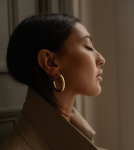 The model stretches her neck back, showing off the large, golden hoop earrings on her ears. 