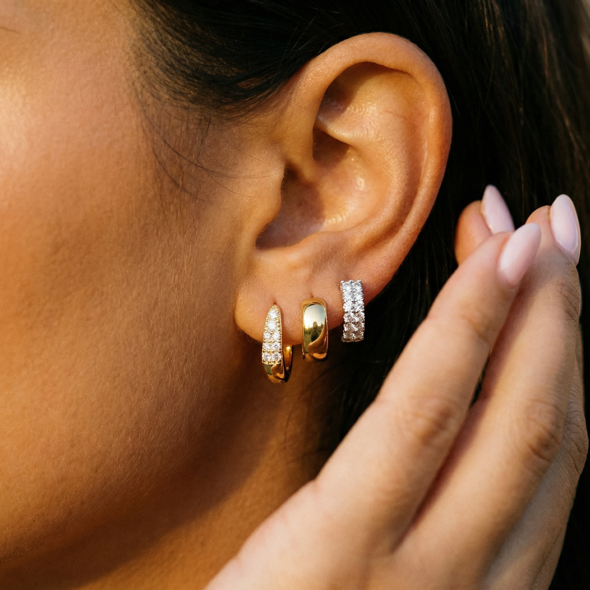 The model stretches to bite a rolled waffle snack, a cocktail before her, and a mini hoop and stud earring stack on her ear.