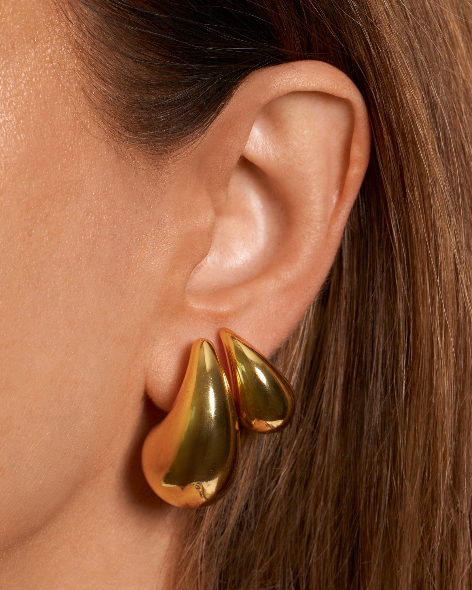 The Moda Hoop Duo is worn in an asymmetrical earring stack where the smaller teardrop of the Moda Hoop Mini lays atop the larger golden curve of the Moda Hoop earring.
