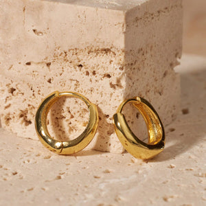 The wide, hollow curve and lever back closure can be seen as a pair of mini Capri Hoop earrings stands propped against a stone block.