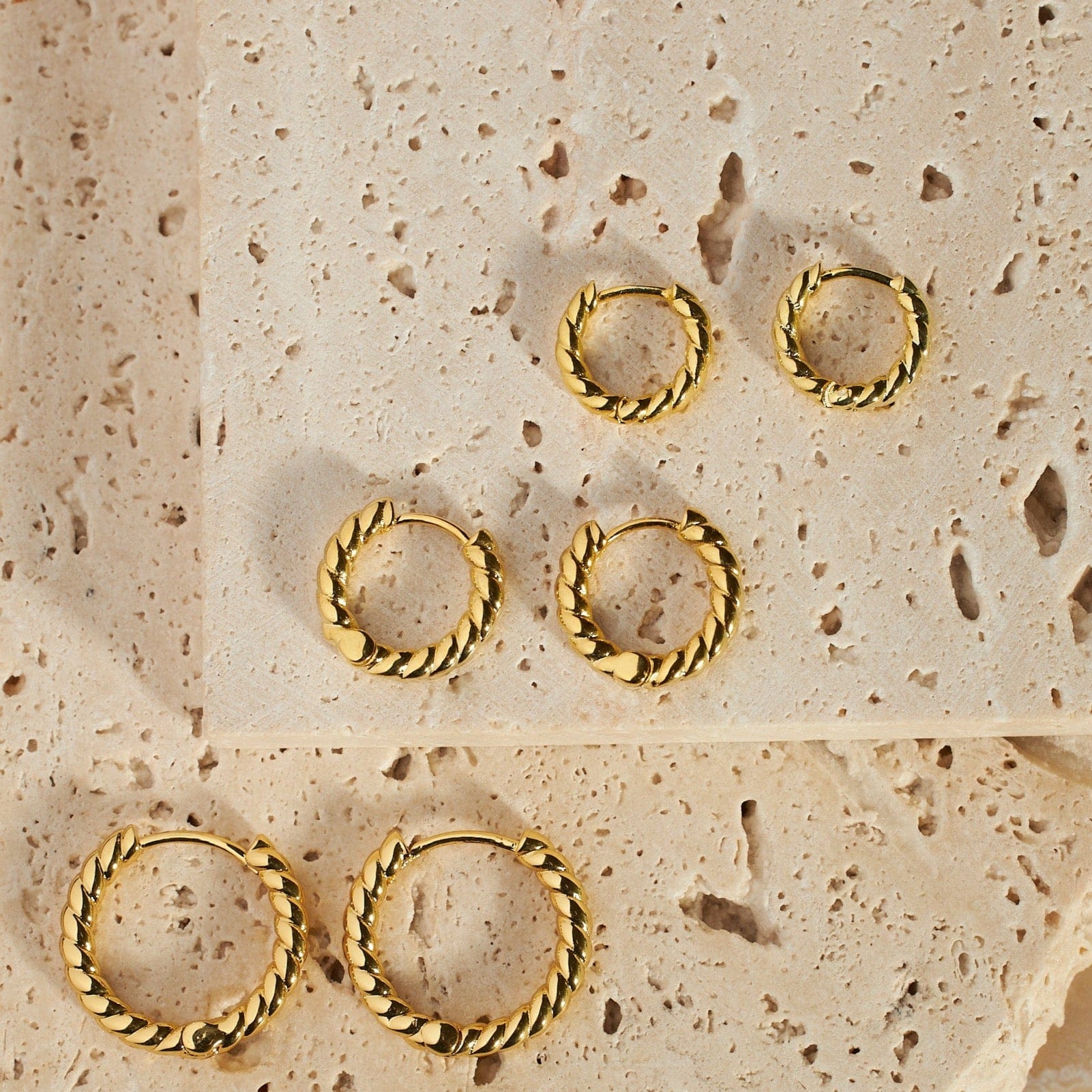 The three pairs of earrings in the Bordeaux Hoop Trio lay on two porous stone slabs, each pair with a different diameter hoop but the same twisted design.  