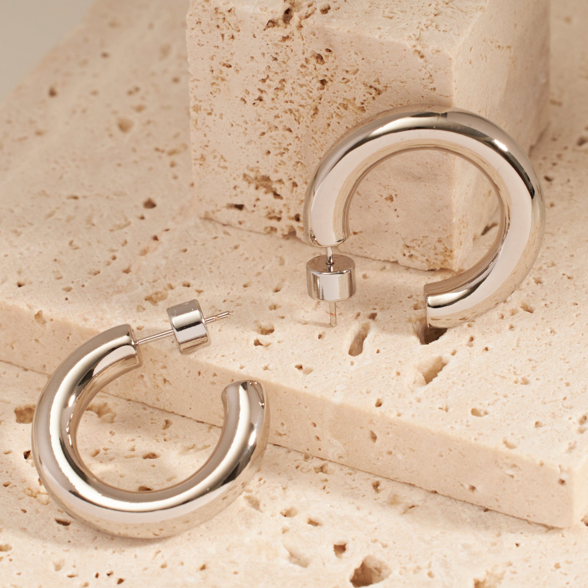 Two platinum Perfect Hoop earrings are displayed side by side, the perfectly round, open hoops reflecting the light on their smooth silver surfaces.