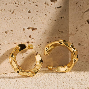 Two Perfect Hoop Marquis earrings show off their golden hammered texture as they stand on their curve, propped up against a stone block. 