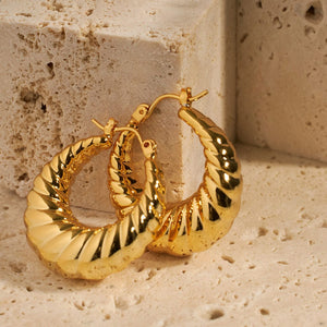 Two Amalfi Hoop earrings show off their oblong shape and vintage design as both earrings are propped up against a stone block, one earring atop the other. 