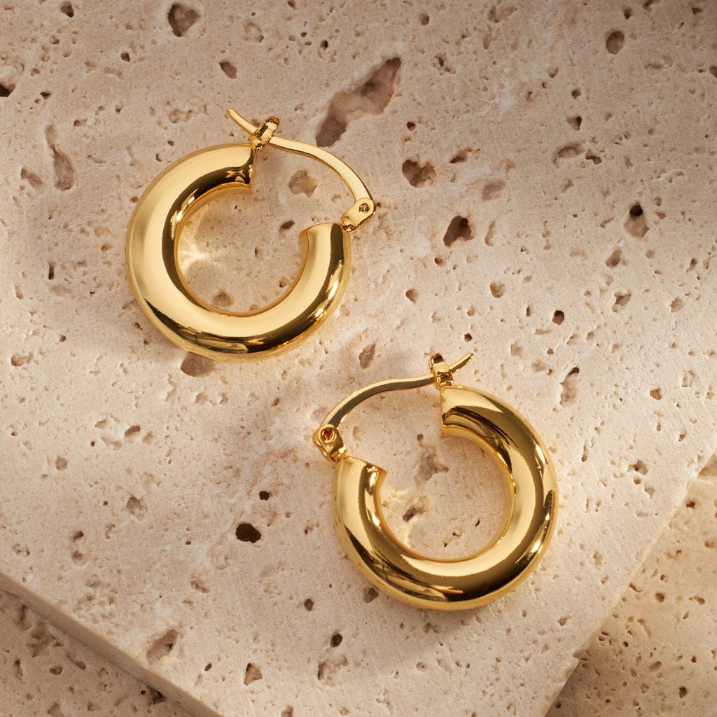Two Saint-Tropez earrings lay adjacently on their sides to show off their smooth golden curves and sleek latch back closures. 