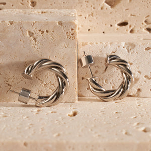 Two Cannes Hoop Mini Platinum earrings are propped up on a counter, each open hoop showing off its twisted design and platinum shine. 