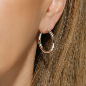 The sterling silver Allegra Hoop Midi glistens in the light as it adorns the model's ear. 