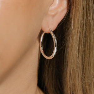 The sleek, sterling silver curve of the Allegra Hoop glistens in the light as its worn on the model's ear. 