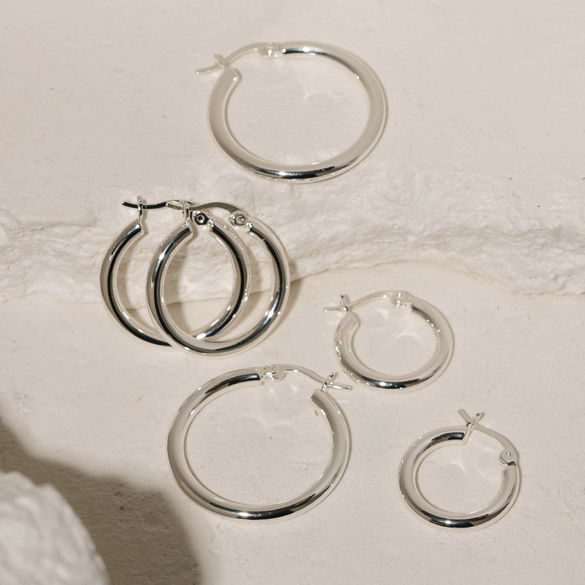 All three earrings in the Allegra Hoop Trio are displayed across some white stone slabs, the silver hoops glistening under the spotlight. 