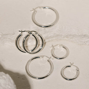 All three earrings in the Allegra Hoop Trio are displayed across some white stone slabs, the silver hoops glistening under the spotlight. 