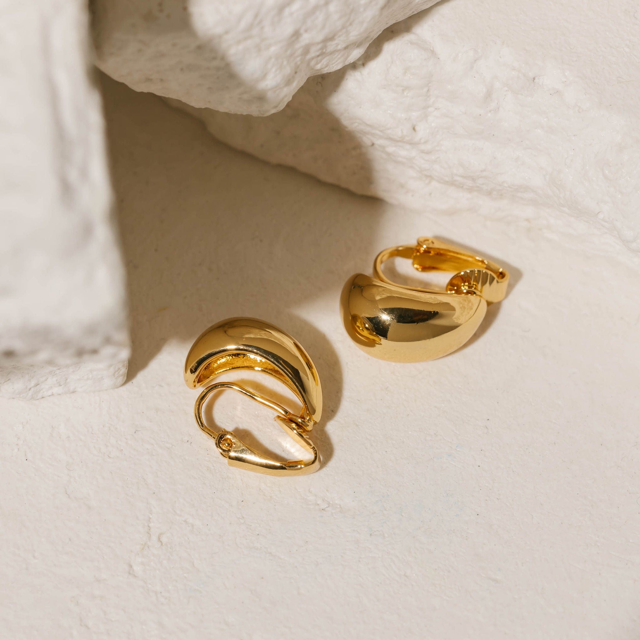 Gold Amadora Hoop Mini Clip-On earrings with a sleek, polished finish, displayed against a textured stone background. These mini clip-on hoops by The Perfect Hoop offer a refined and versatile style, perfect for everyday wear