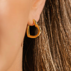 The Amore Hoop Mini on the model's ear hangs gracefully at an angle as the golden curves glisten. 