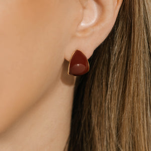 Model wearing The Cabernet Hoop earrings, showcasing a deep red enamel finish in a soft triangular design framed in gold, offering a sophisticated and striking look.