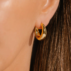 The sleek, golden curve of the Capri Hoop Midi earring glisten on the model's ear. 