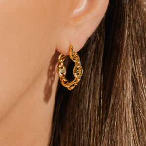 The golden links of the Cavalla Hoop shine in the light as the earring adorns the model's ear. 