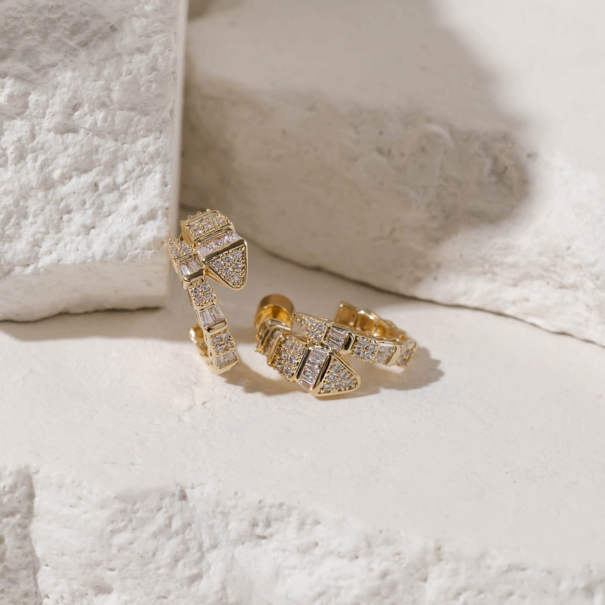 Two Diana Hoop earrings sit together on stone slabs, their crystal accents shinning along the serpentine design. 