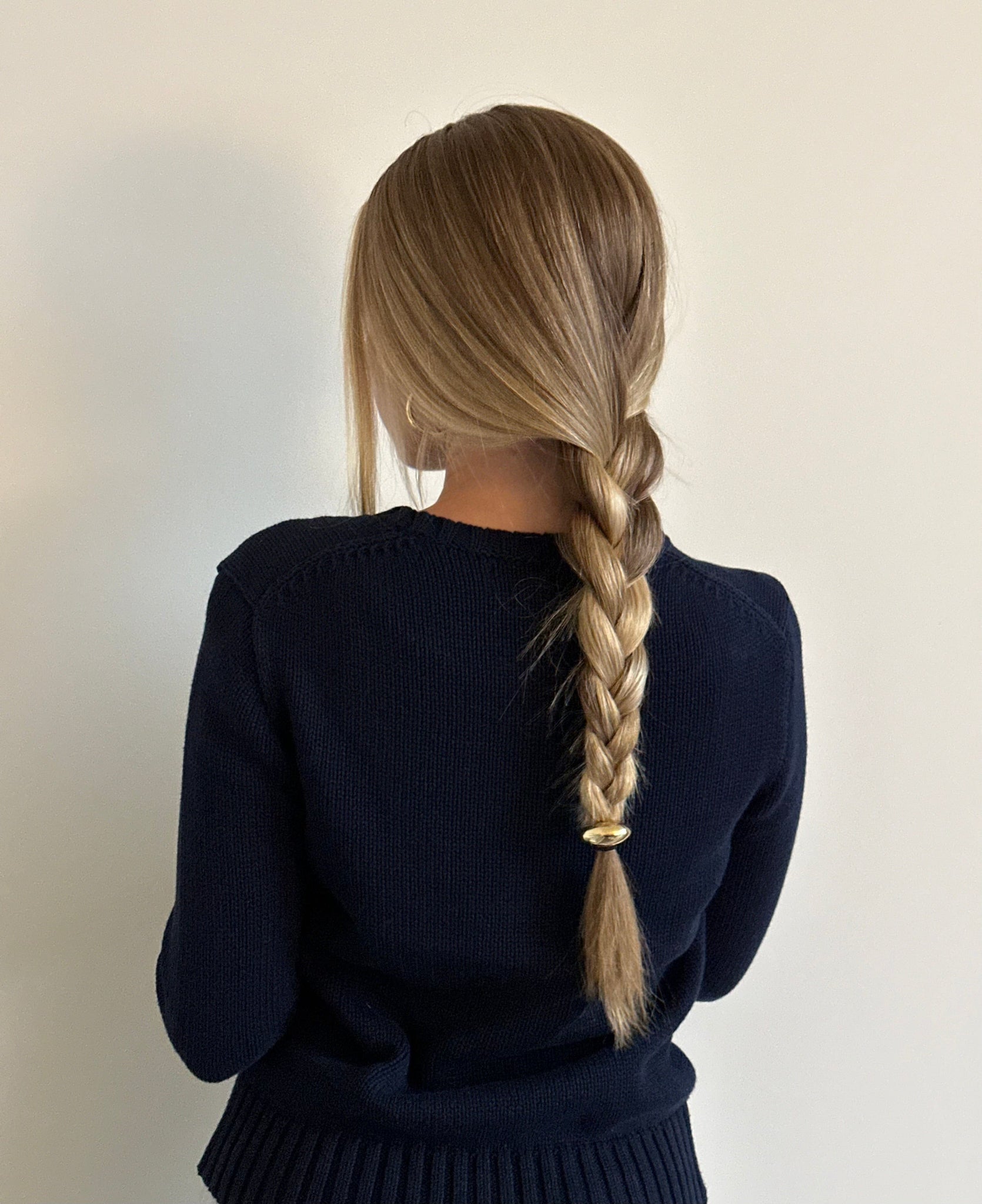 Blonde model wearing The Perfect Hair Hoop Mini in gold at the end of a braid, styled with a black sweater for a minimal, polished look