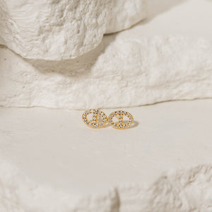 The Jolie Stud pavé earrings in gold, featuring a delicate circular design encrusted with sparkling crystals, displayed on a natural stone background. Gold pavé stud earrings by The Perfect Hoop.