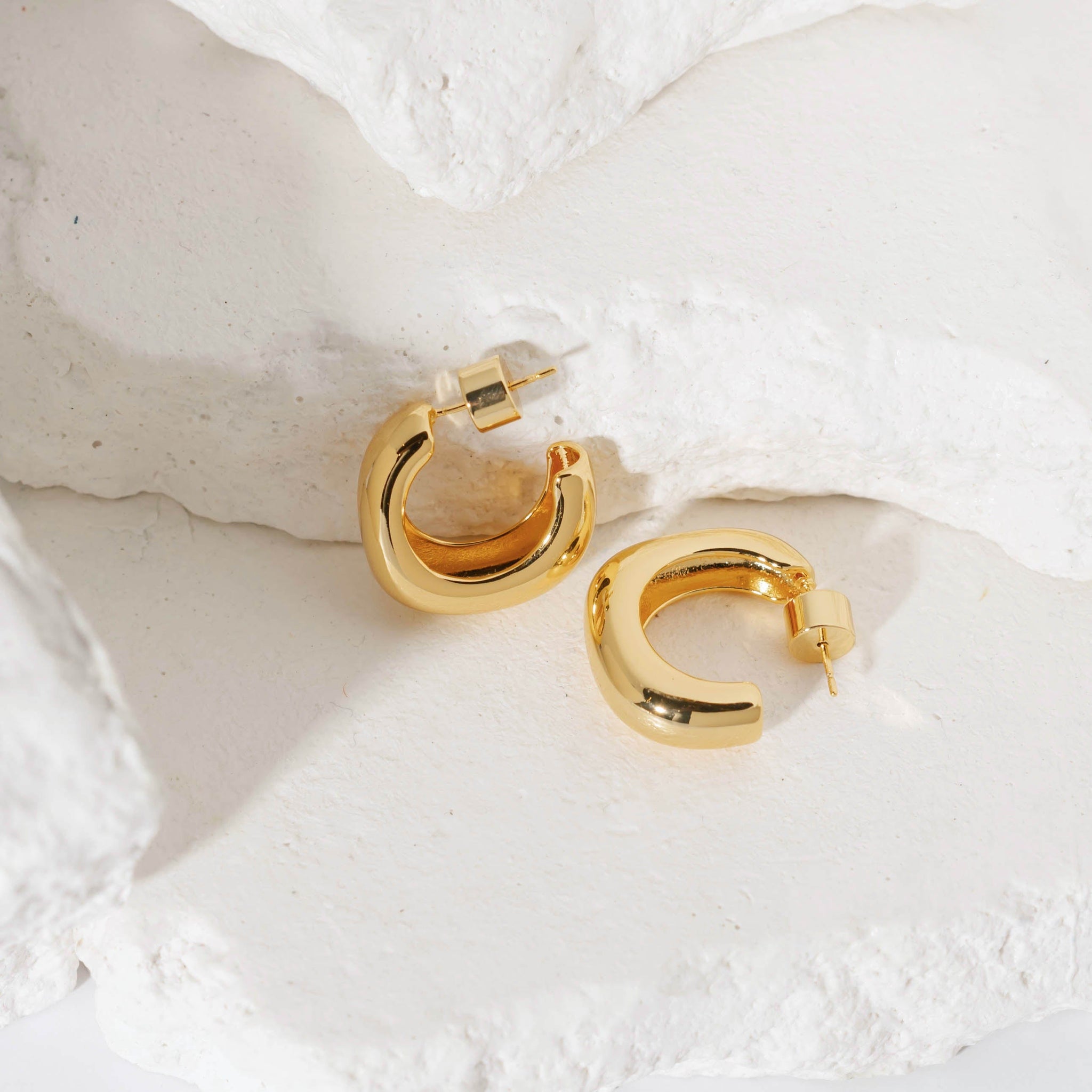 "Gold Le Mans Hoop earrings with a bold, open design and smooth polished finish, displayed against a textured stone background. These elegant hoop earrings by The Perfect Hoop offer a modern and sophisticated look