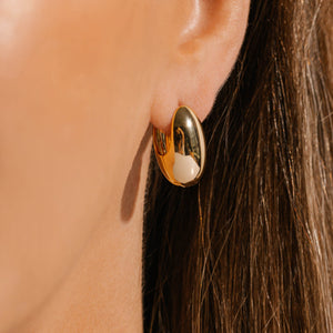 The smooth, golden surface of the Lisbon Hoop earring reflects its surroundings as it adorns the model's ear. 