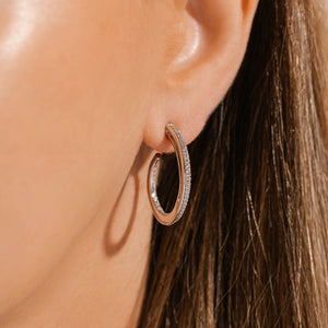 The model wears the Luxe Hoop earring, a front perspective showing the smooth, asymmetrical inner curve and the outward-facing crystal accents. 