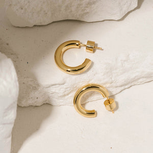 The Malta Hoop 20 mm gold earrings styled on white stone with subtle reflective lighting.  By The Perfect Hoop.