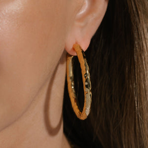 Model wearing The Marbella Hoop 50 mm in gold with a hammered finish, casting a soft shadow on the cheek. Styled with sleek brunette hair.  By The Perfect Hoop.