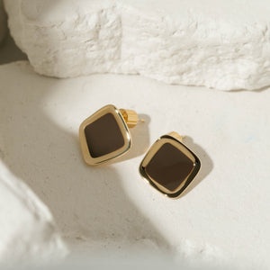 The Mochachino Hoop earrings with a glossy mocha-brown enamel finish and a gold-framed soft square design, displayed on a textured stone surface for a sophisticated touch.