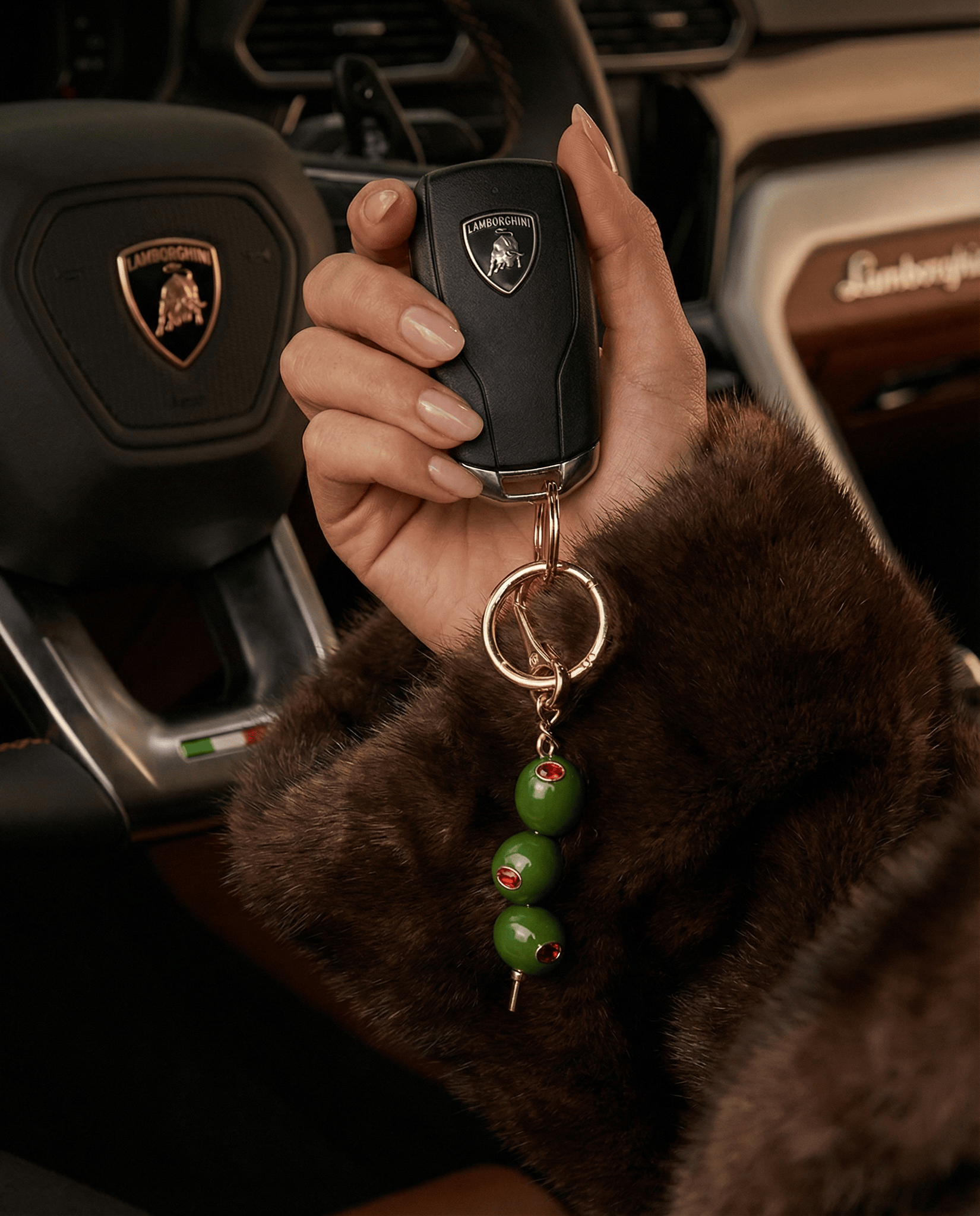The Perfect Hoop The Extra Dirty Keychain with green olive bead charms and red crystal accents, attached to car keys and held in hand inside a luxury car, styled as a lifestyle shot.