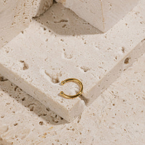 The Perfect Cuff lays on a tiered stone surface, showing off its open hoop design and smooth golden finish. 