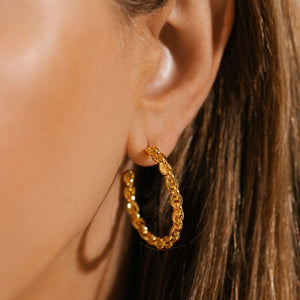 The open Catena Hoop earring adorns the model's ear, the golden chainlink hoop shining where it catches the light.