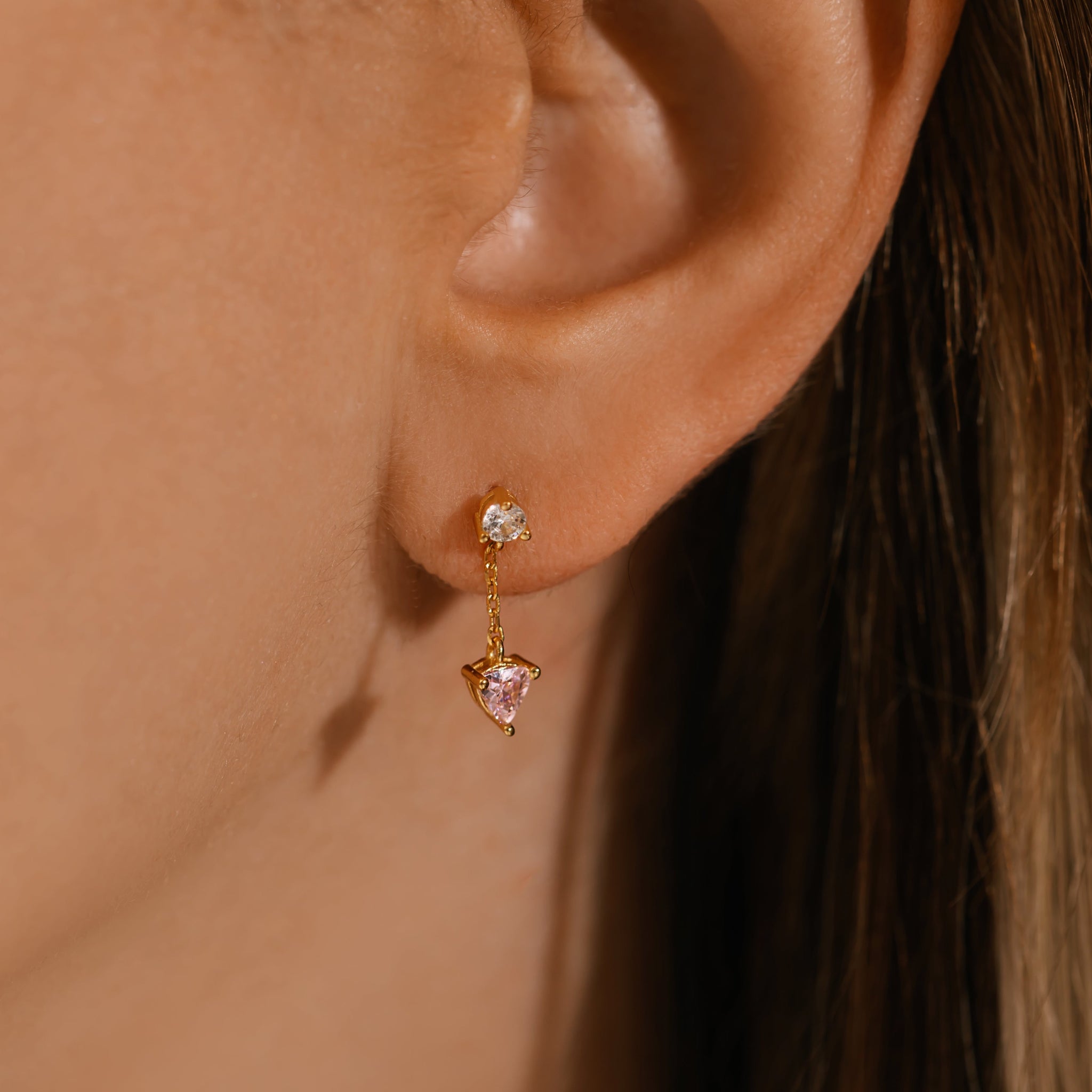 A close-up view of the Bambina Chain Drop earring on the model's ear, the larger pink crystal gracefully dangling from a delicate golden chain that's connected to the smaller, clear crystal stud. 