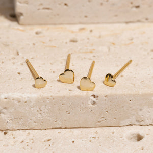 The two pairs of earrings in the Amore Stud Duo lay side-by-side on a stone slab, showing off the difference in sizes and golden, heart-shaped design. 