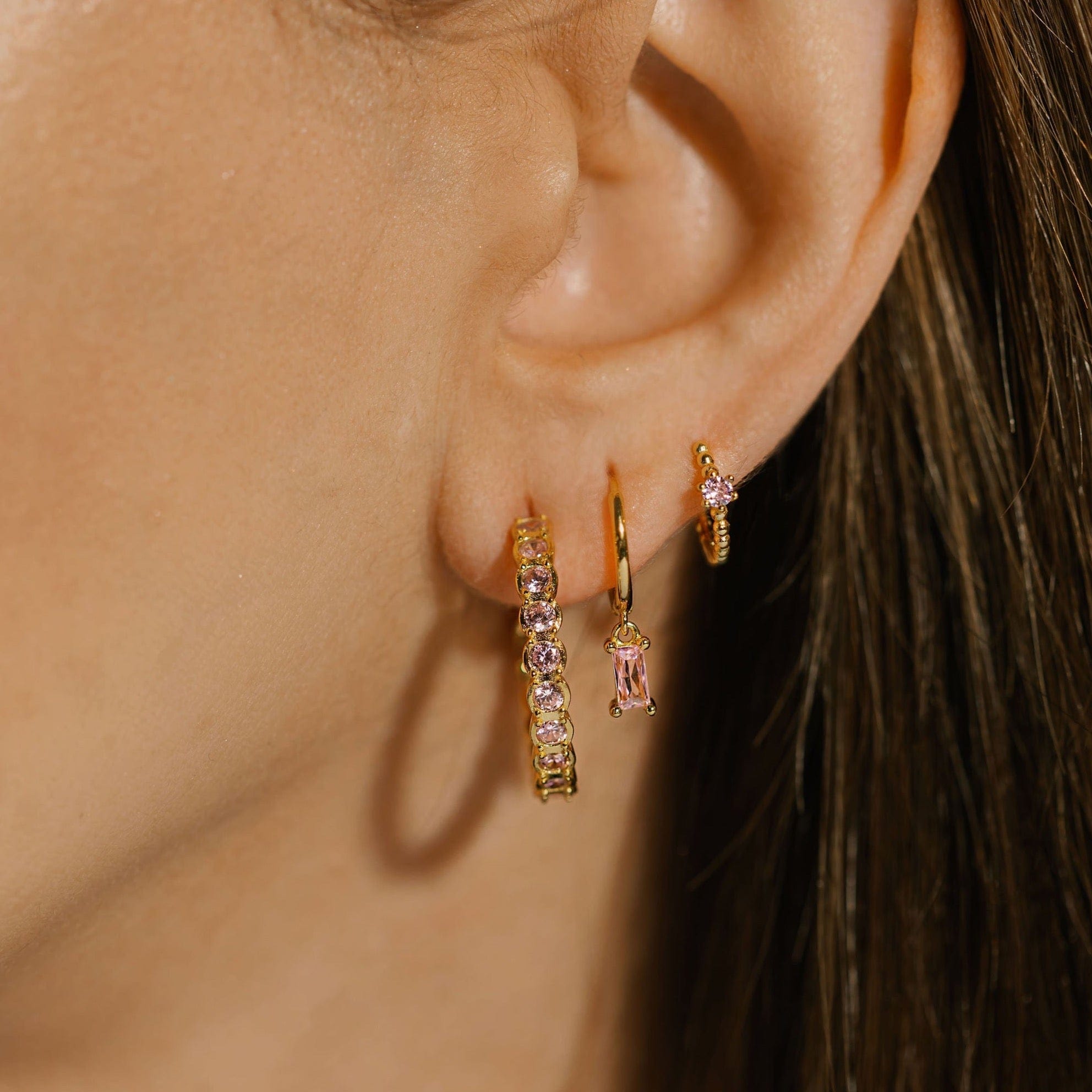  A close-up view shows the complete Bambina Hoop Trio earring set worn in a glamorous stack. The unique style and sparkling pink crystal accents give this elegant trio a quirky touch. 