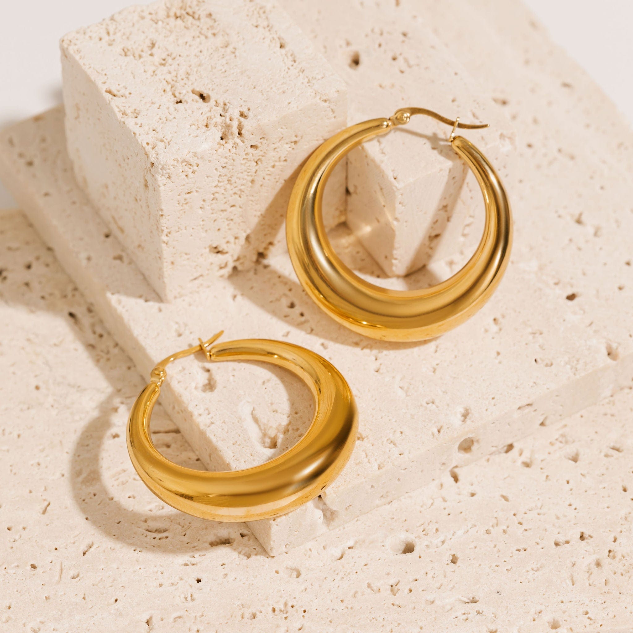 A pair of Capri Hoop Grande earrings is displayed on a counter, the smooth, crescent shape of the hoop shining golden under the light. 