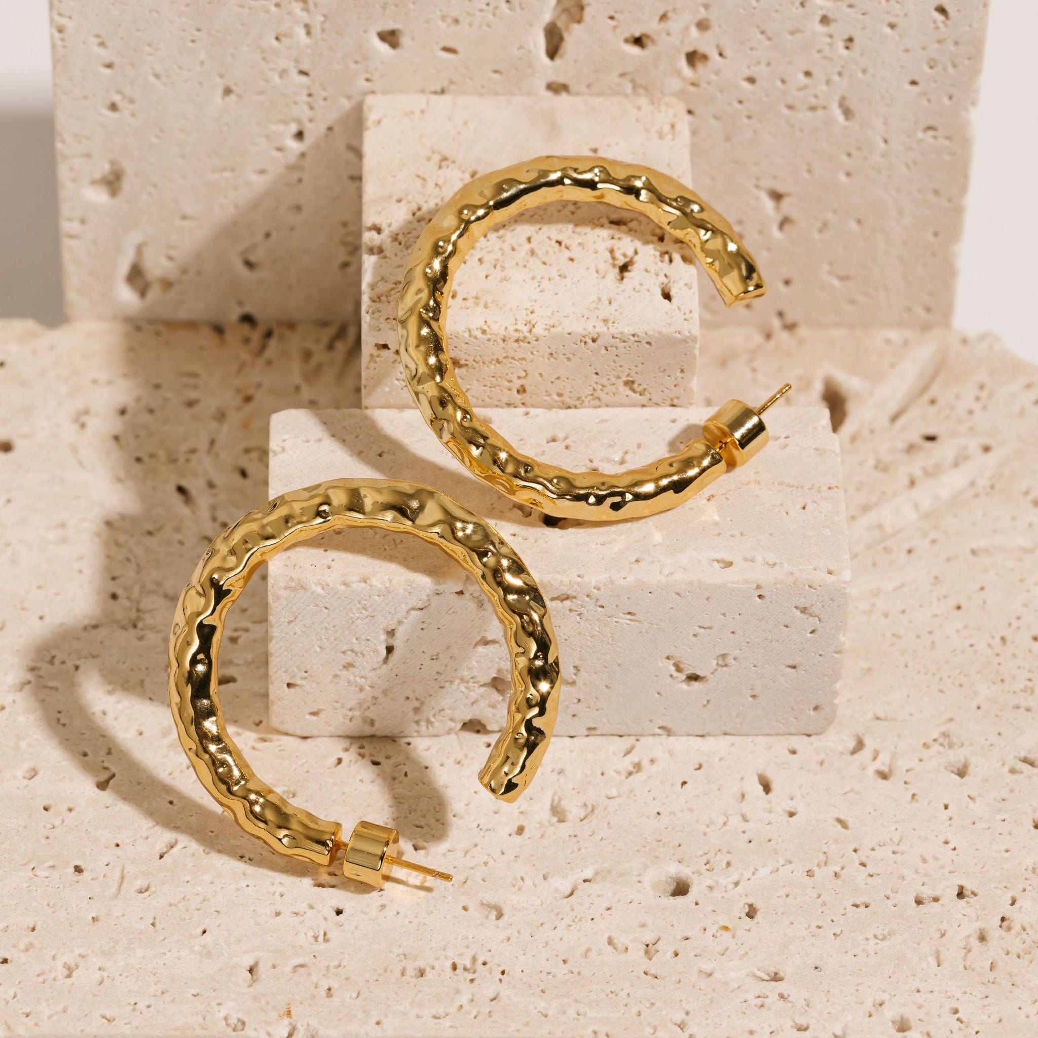  Two 40mm Marbella Hoop earrings are propped up and displayed side-by-side to show of their open-hoop shape and hammered texture.