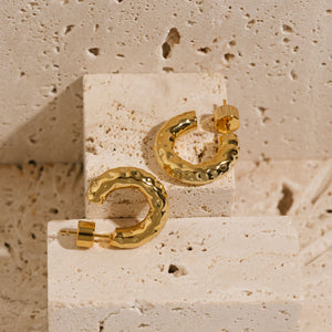 A pair of 20mm Marbella Hoop earrings is displayed on a stone slab to show off the slightly hammered texture and open hoop design.