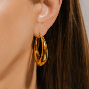 The bold face of the Capri Hoop Grande glistens and reflects the room in a close-up view of the earing on the model's ear. 