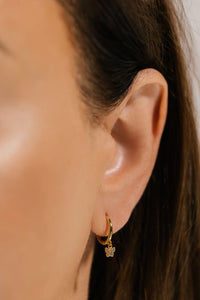 The dazzling butterfly charm of the Mariposa Drop Hoop dangles delicately from the golden hoop as it's seen in a close-up view of the model's ear. 