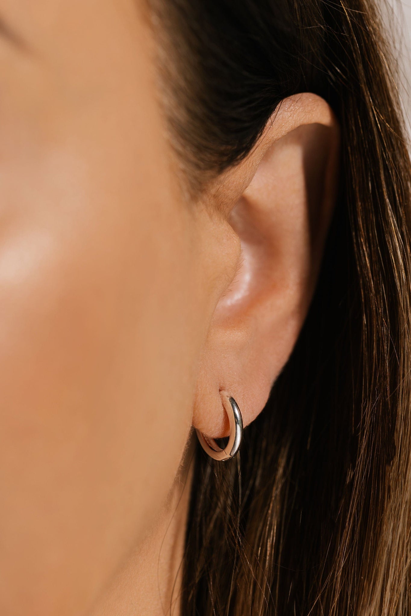 A close-up view shows the dainty Ravello Huggie in sterling silver gracefully curving around the model's ear lobe. 