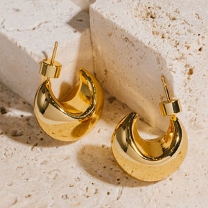Two Córdoba Hoops sit side by side next to a pair of stone blocks, the hoops resting on their broad, crescent-shaped curves as the pushback closures extend upward.