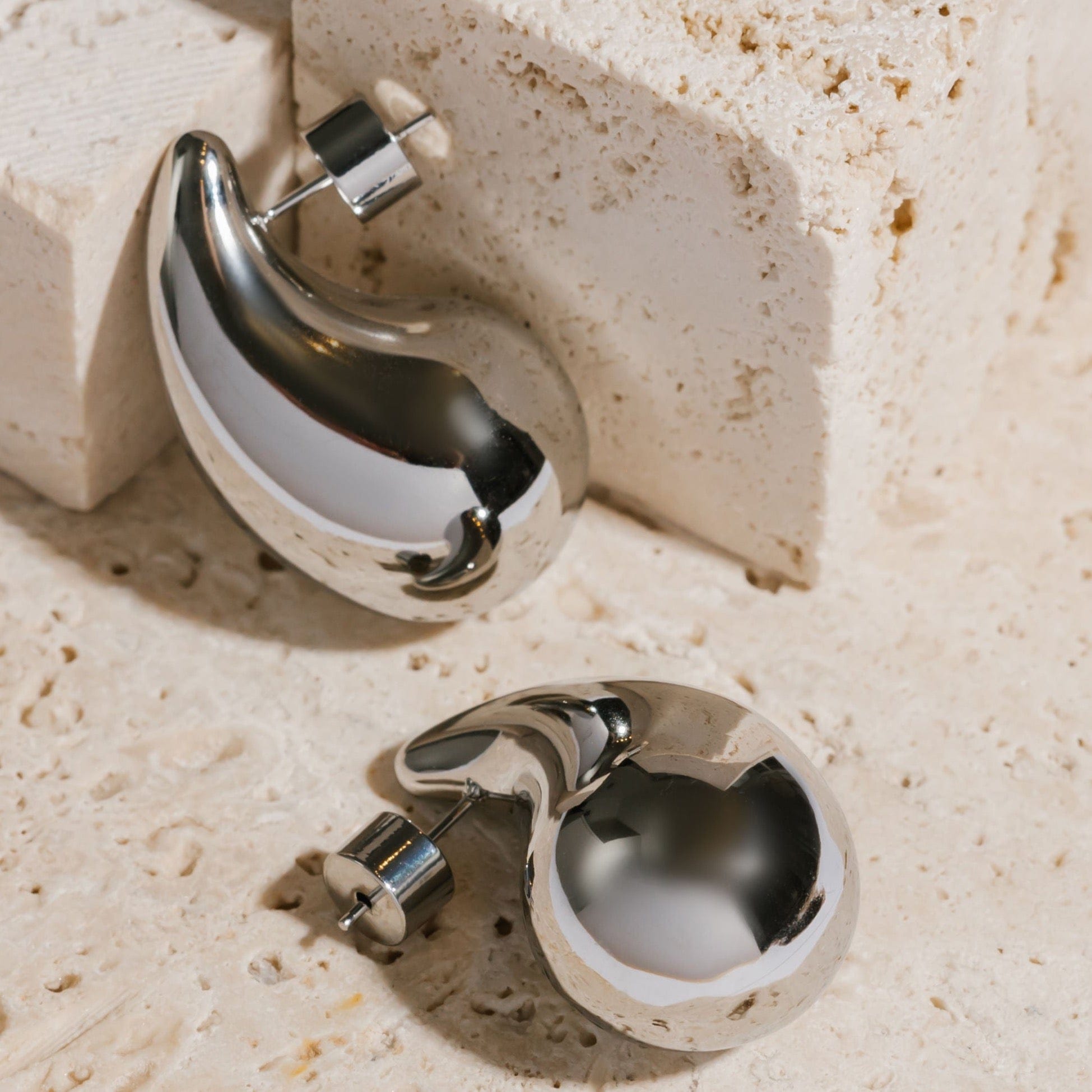 A pair of platinum Moda Hoop earrings lay side-by-side on a stone slab, the smooth platinum surface reflecting its surroundings. 