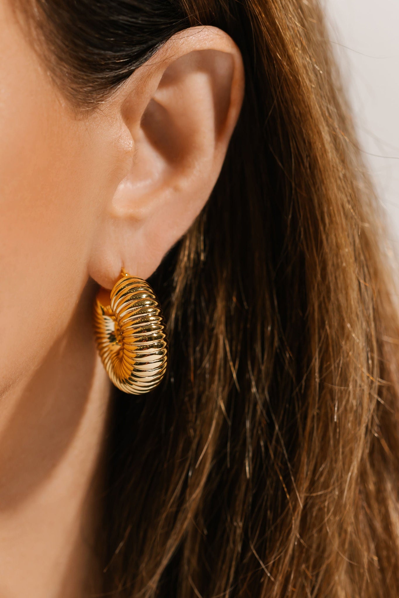 A golden Brioche Hoop decorates the model's ear with its bold and stylish ribbed design. 